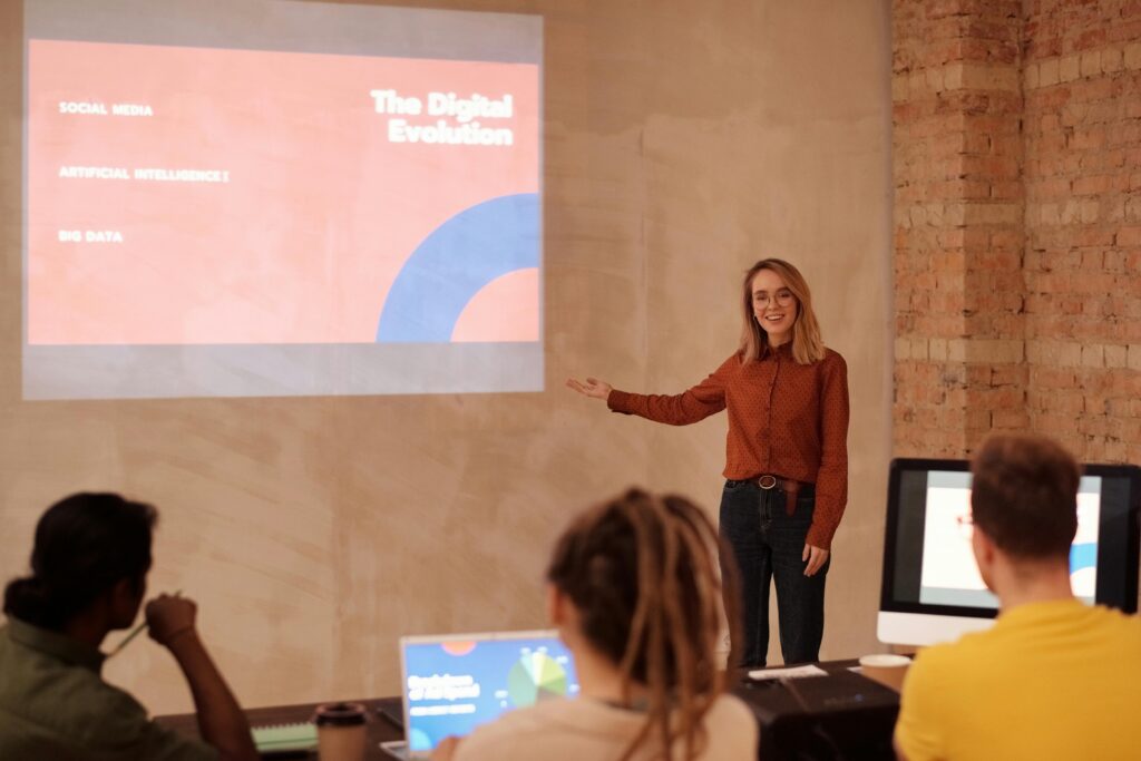 A woman standing and giving a professional presentation in a workplace setting.