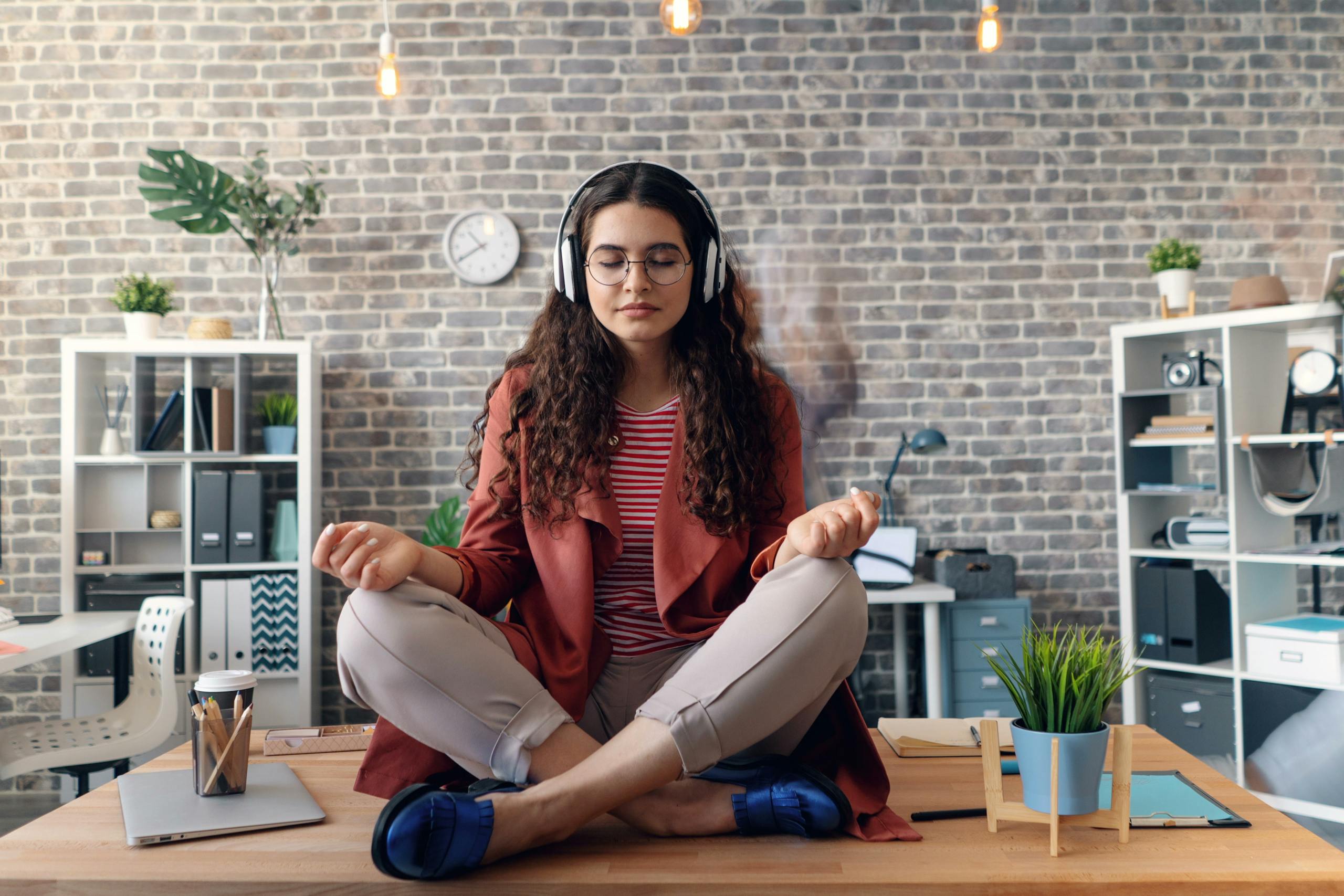 A woman meditating on top of a desk in the office.